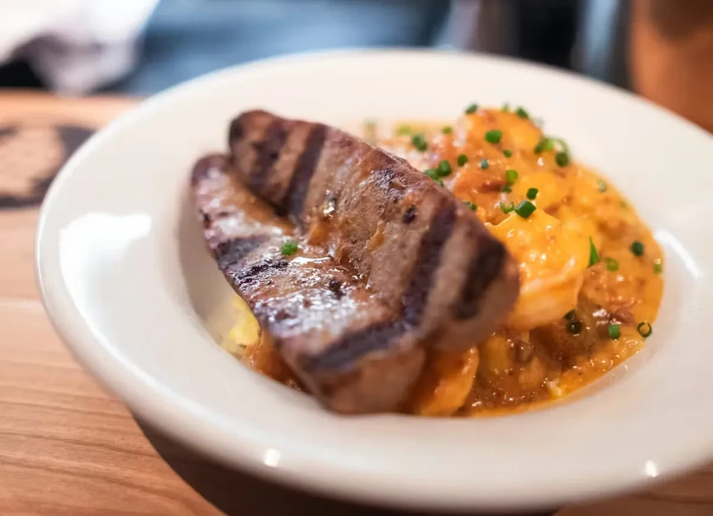 Grilled meat with grill marks on creamy orange shrimp sauce and chives.