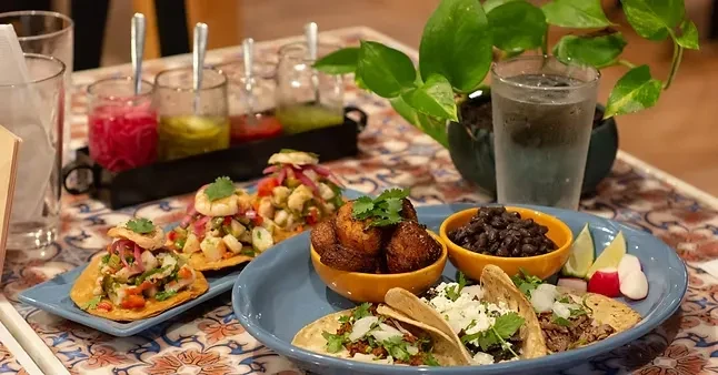 Colorful restaurant spread of seafood tostadas, meat tacos, beans, and plantains.