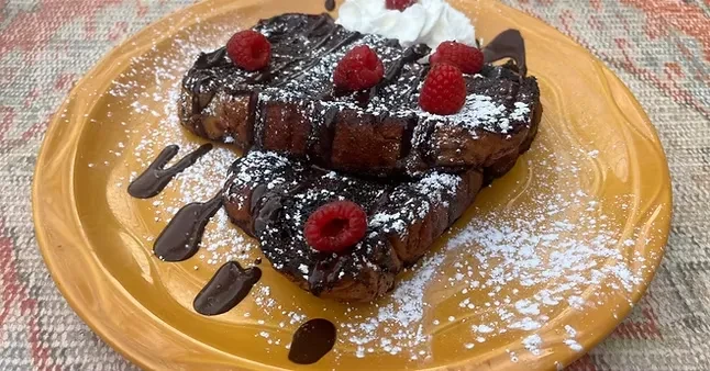 Stacked French toast with chocolate, raspberries, powdered sugar, and whipped cream.
