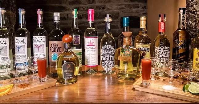 Mezcal and tequila bottle display with tasting setup on rustic wood.