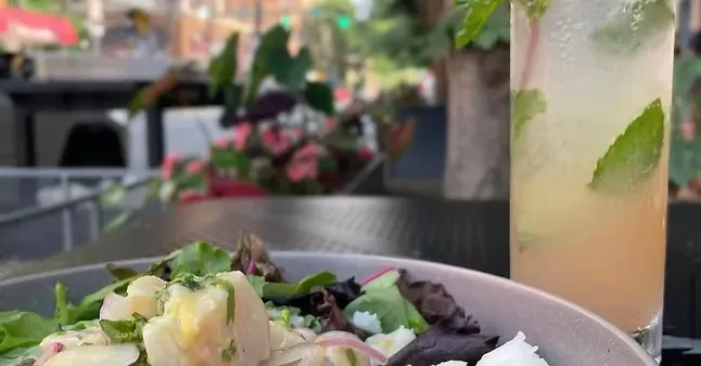 Close-up of fresh salad bowl and iced mint drink outdoors.