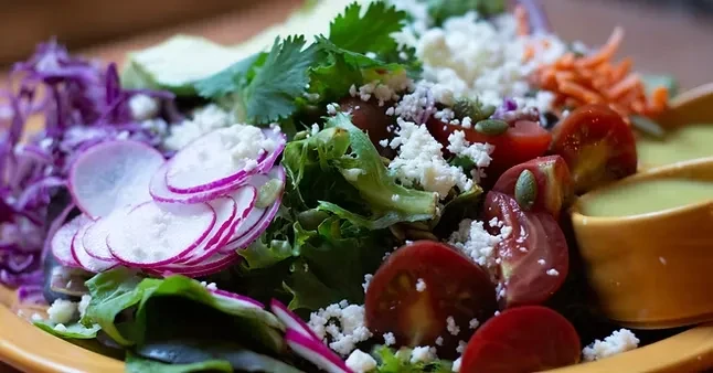 Colorful salad with lettuce, radishes, tomatoes, cheese, and side dressing.