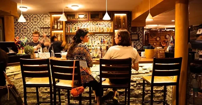 Cozy bar interior with two women, a bartender, and warm lighting.