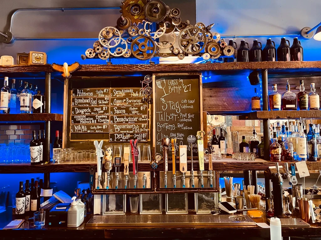 Well-stocked bar with steampunk gears, blue light, multiple beer taps.