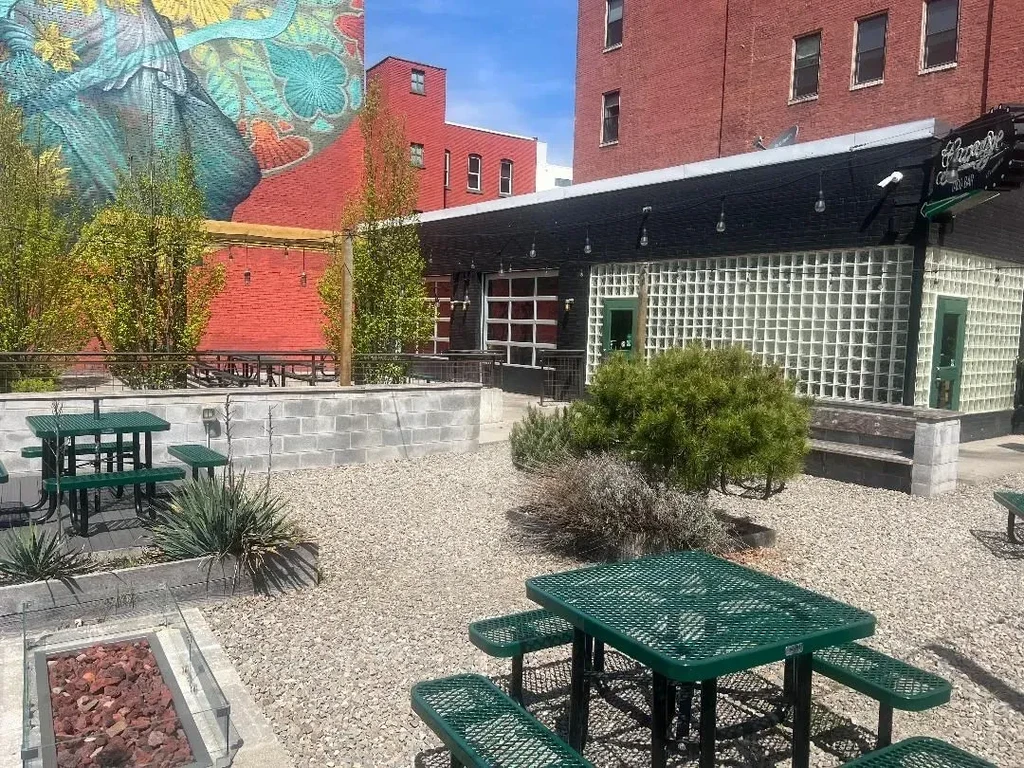Outdoor restaurant patio with green tables, fire pit, and colorful mural.