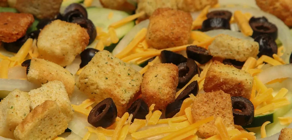 Close-up salad with croutons, black olives, cheddar cheese, and cucumber.