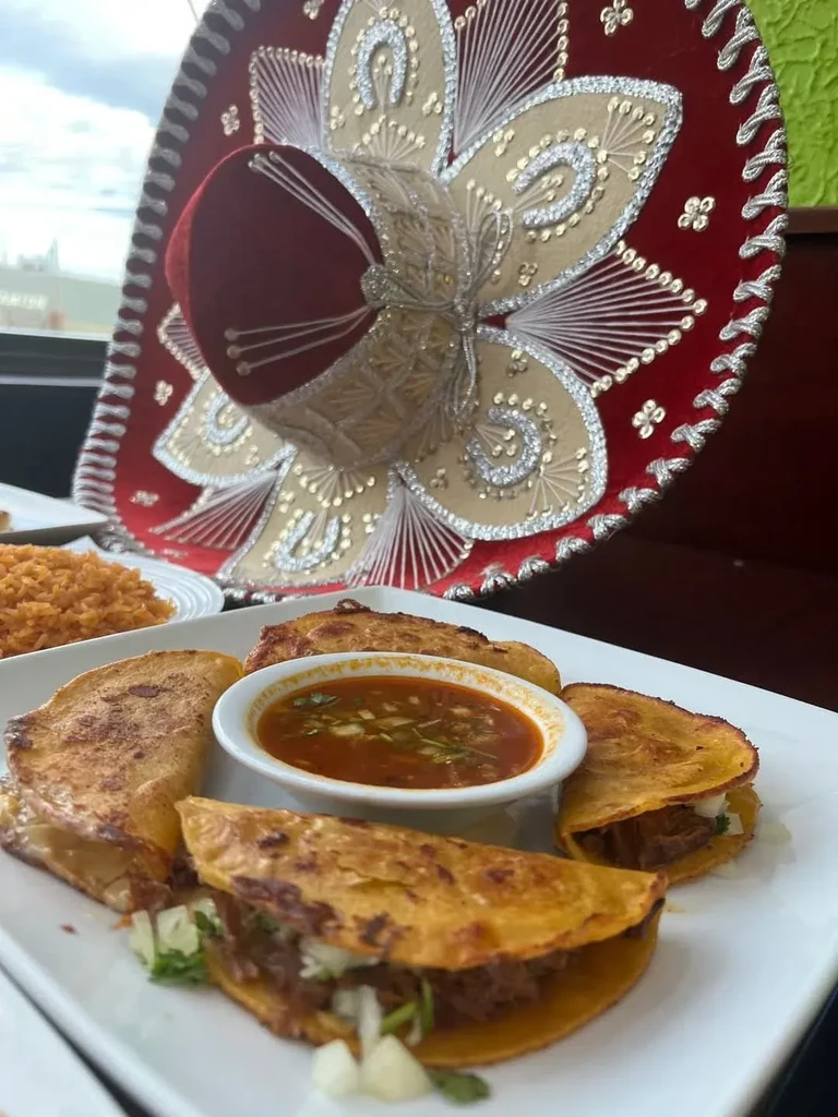 Birria tacos, consommé, and Mexican rice with a decorative red sombrero.