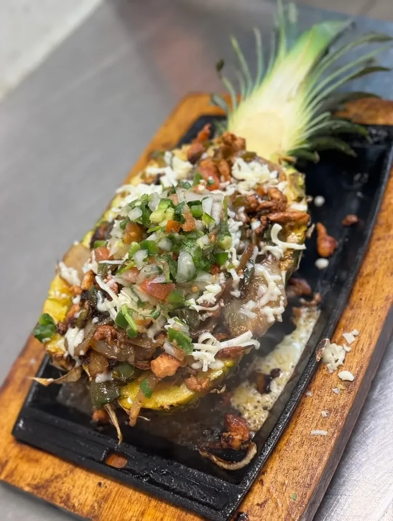 Pineapple half filled with sizzling meat, peppers, cheese, and salsa.