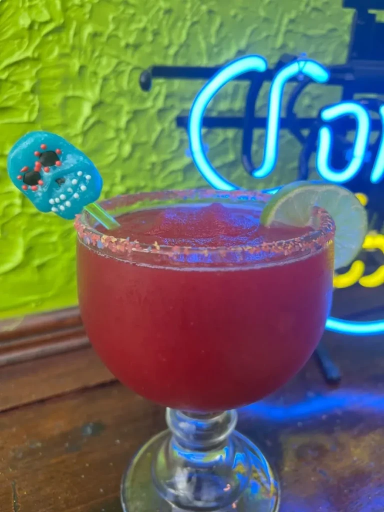 Frozen red drink with chili-lime rim, lime, and sugar skull pick.