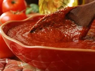 Close-up of thick red tomato sauce with a spoon and fresh tomatoes.