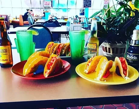 Plates of tacos, beers, and drinks in a casual Mexican restaurant.