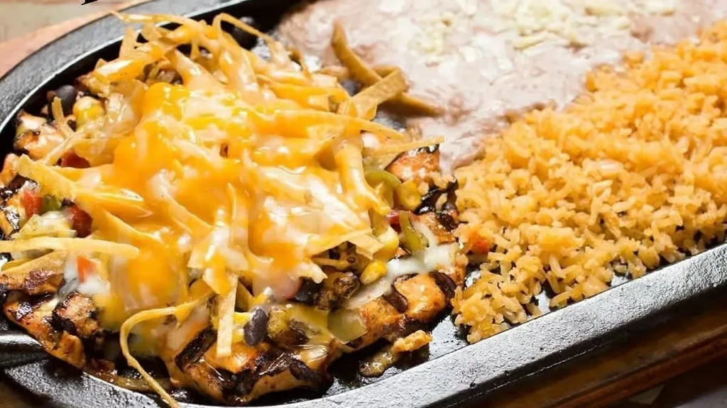Sizzling Mexican platter: grilled meat, vegetables, cheese, rice, and beans.