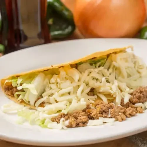 Hard-shell taco filled with meat, lettuce, and cheese on white plate.