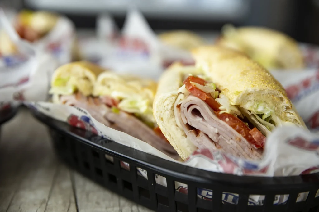 Two generously filled deli subs with meat, tomato, and lettuce.