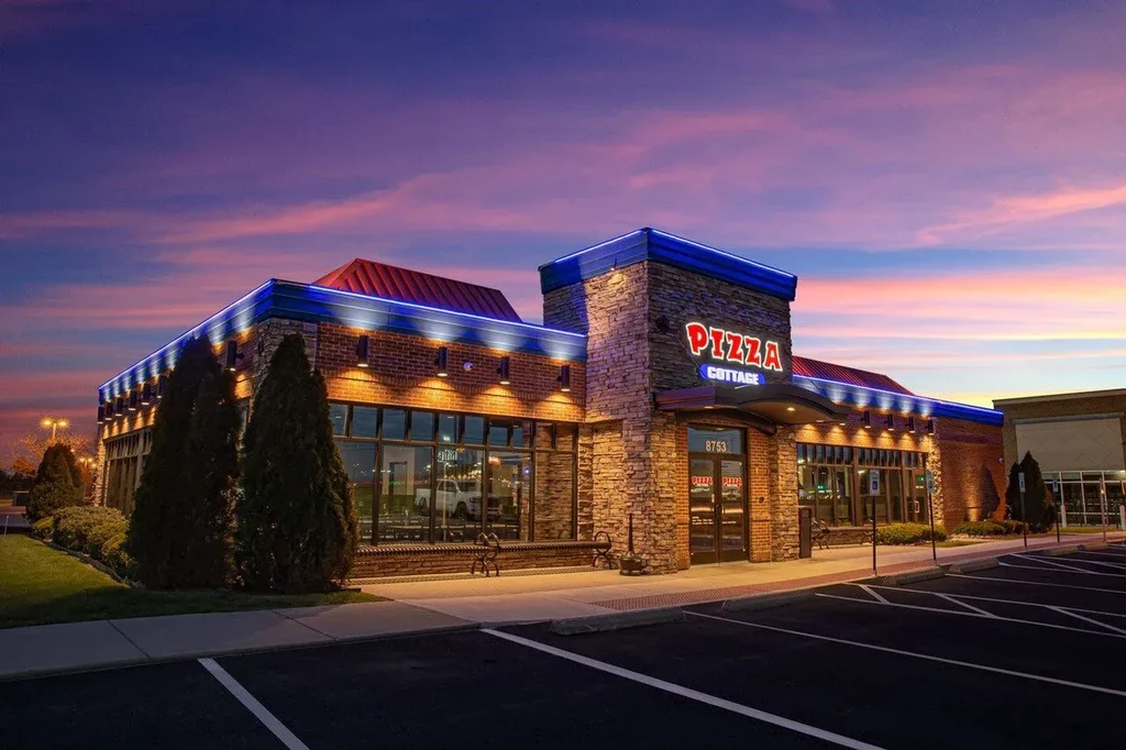 Pizza Cottage exterior at dusk, illuminated by colorful sunset and blue neon.