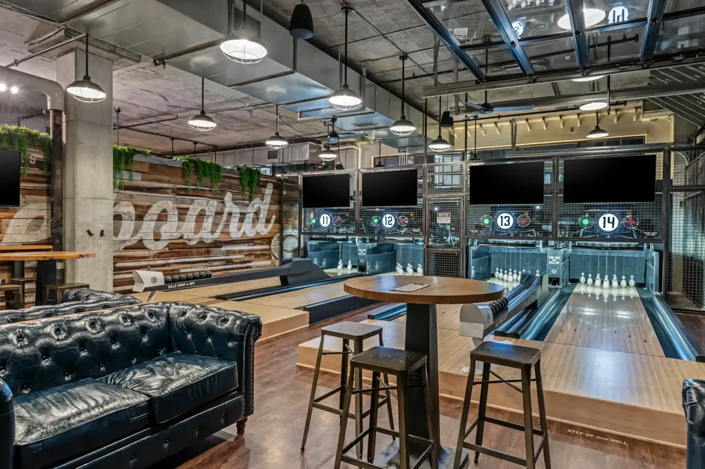 Industrial-chic bowling alley with lanes, lounge, and a "Board" sign.