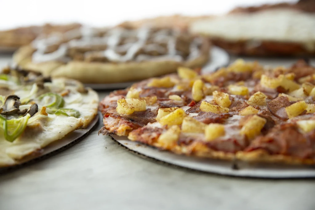 Foreground Hawaiian pizza among several other pizzas on a counter.