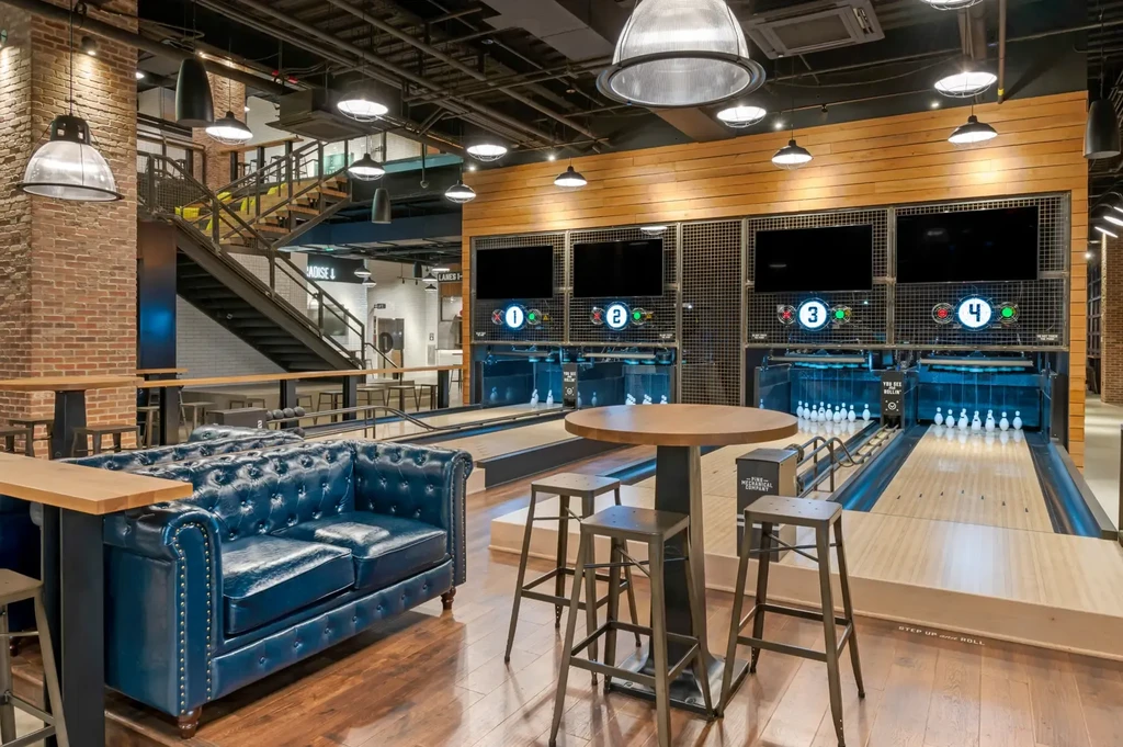 Modern industrial lounge with Chesterfield sofa and bowling lanes.