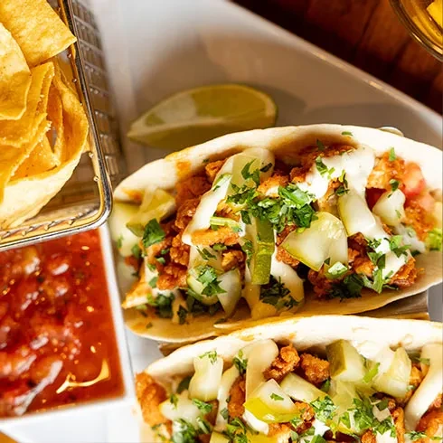 Two meat tacos, tortilla chips, red salsa, and lime, top-down view.