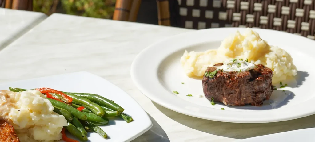 Two plates of seared steak, mashed potatoes, and green beans.