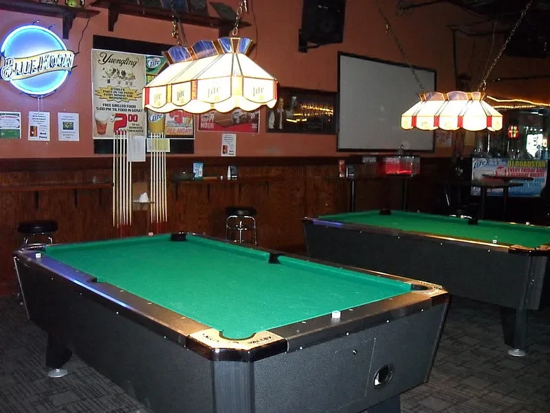 Two green pool tables with stained-glass lamps in a dim bar.