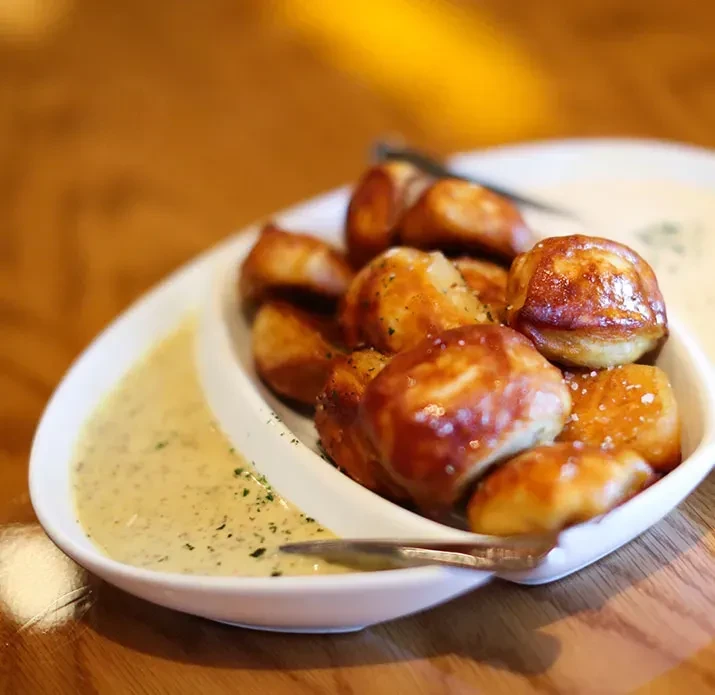 Irregular white dish of salted pretzel bites with two dipping sauces.