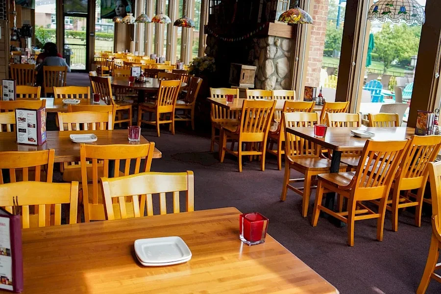 Bright restaurant dining area, wooden tables, chairs, stained-glass lights, patio view.