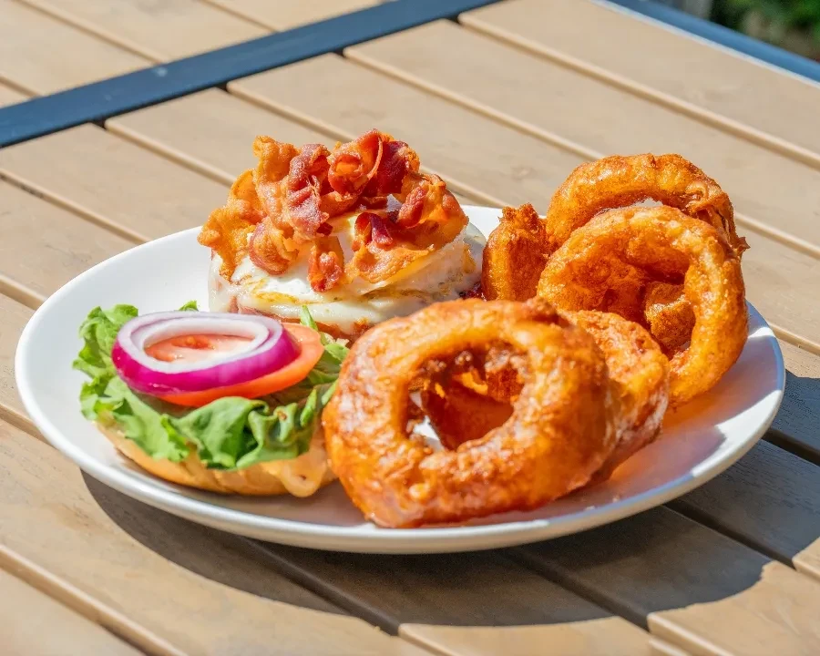 Open-faced burger with bacon, lettuce, tomato, and golden onion rings.