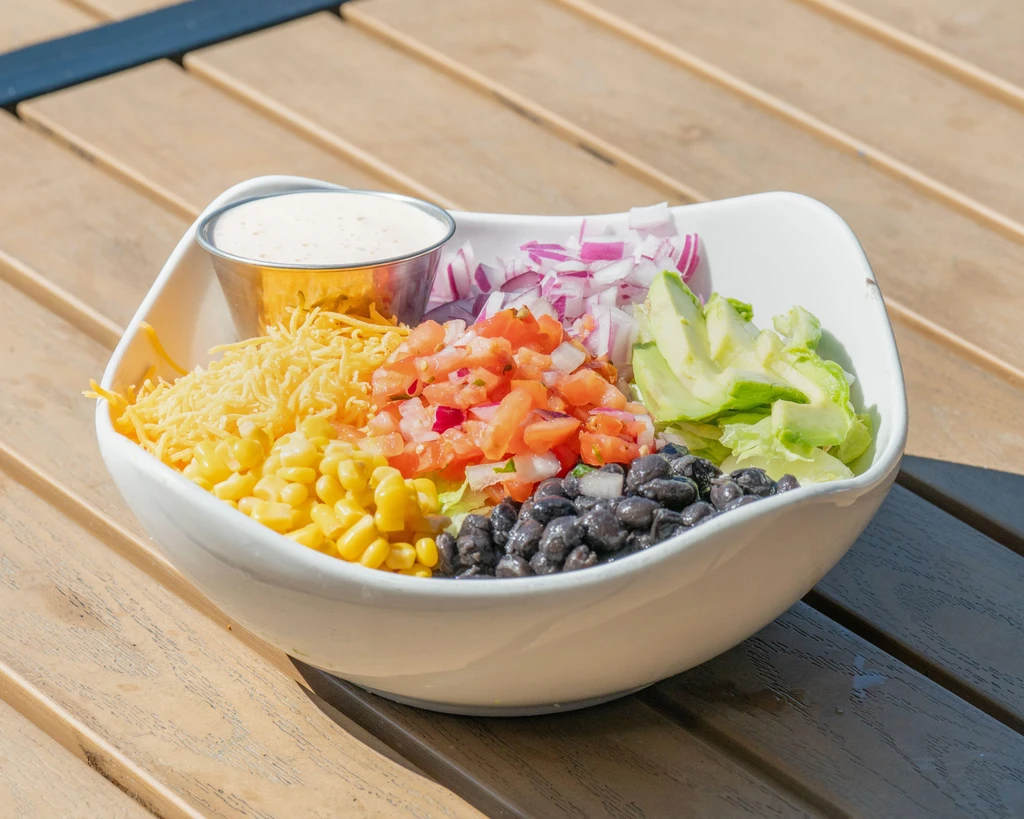 Colorful salad in a white bowl with dressing on a wooden table.