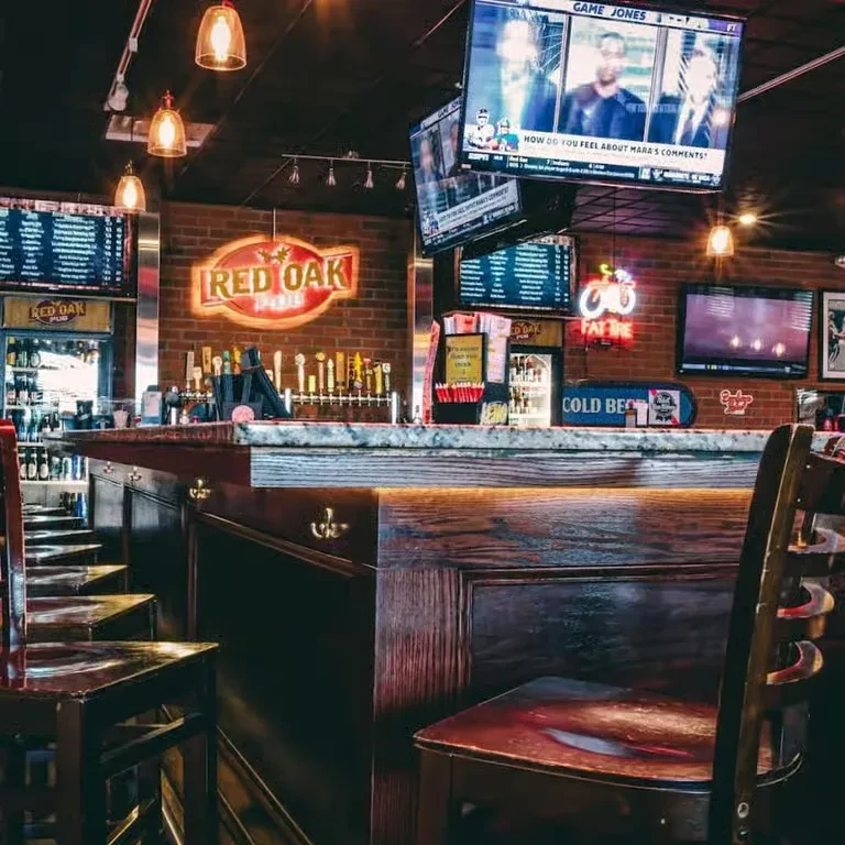 Warmly lit Red Oak Pub bar with stools, taps, and TVs.