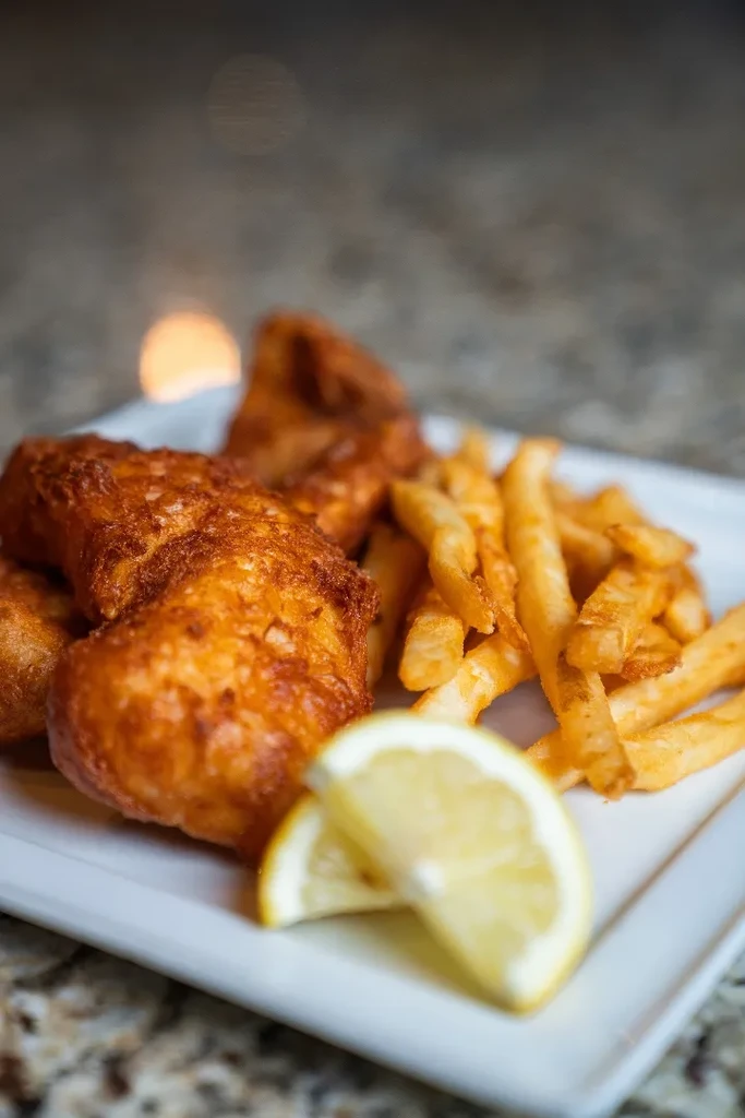 Plate of golden fish and chips with lemon wedges on a white plate.