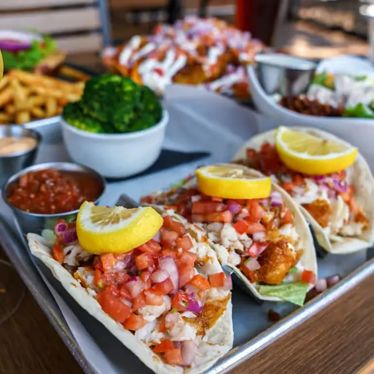 Close-up of three garnished fish tacos with salsa, broccoli, and fries.