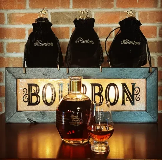 Blanton's bourbon bottle, glass, "BOURBON" sign, and horse-topped velvet bags.