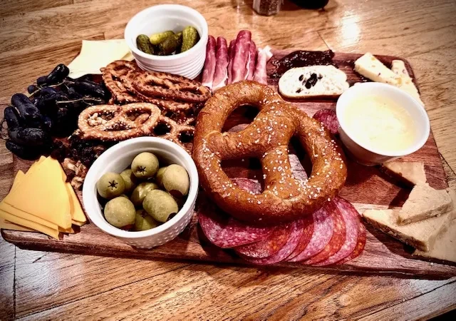 Overhead wooden charcuterie board with meats, cheeses, pretzels, and grapes.