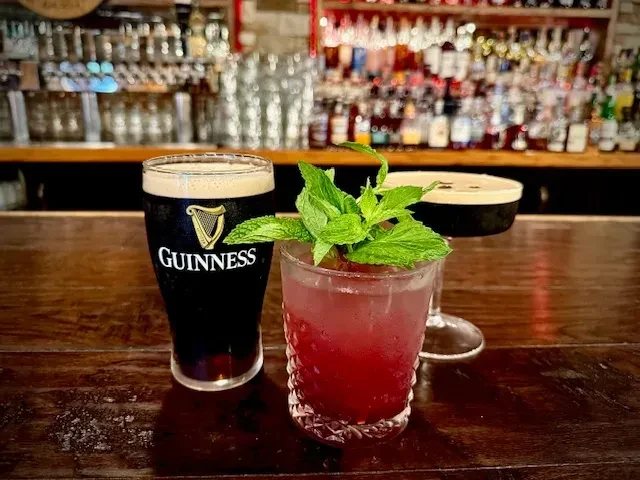 Guinness beer, red cocktail, and dark cocktail on a wooden bar.