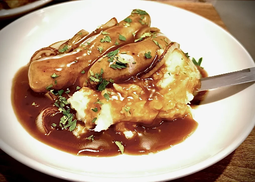 Sausages, mashed potatoes, and brown gravy garnished with herbs and onions.
