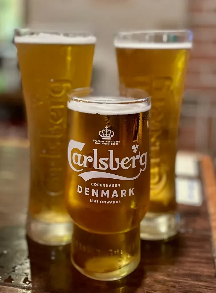 Three Carlsberg beers, foamy and condensed, on a wooden surface.