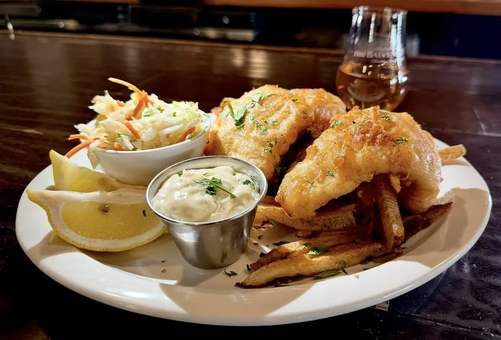 Fried fish, thick-cut chips, coleslaw, tartar sauce, and lemon wedges.