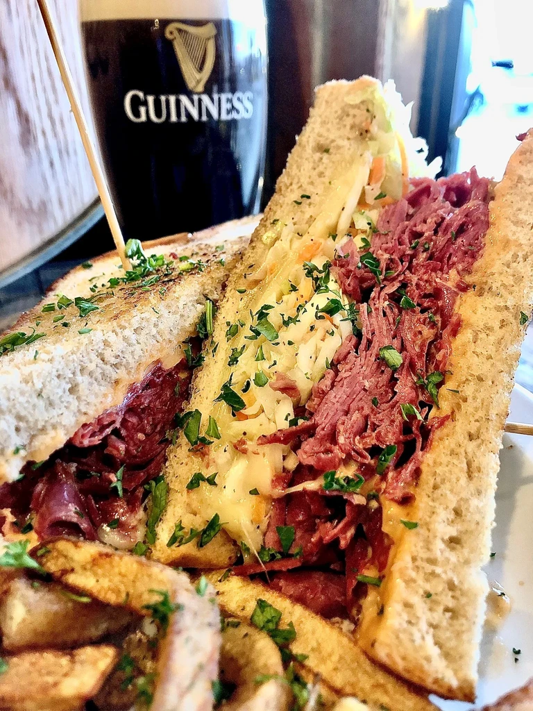 Hearty Reuben sandwich, fries, and a Guinness pint in a pub setting.