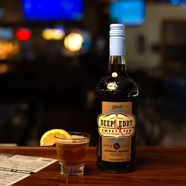 Deep Eddy Sweet Tea Vodka bottle and a lemon-garnished drink on a bar.
