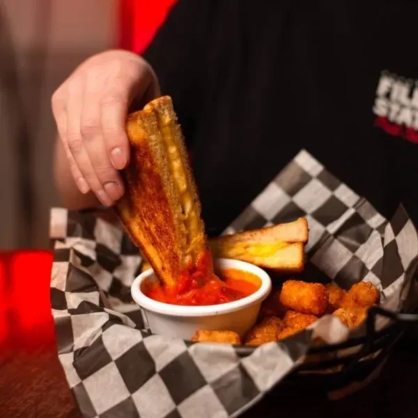 Hand dips crispy grilled cheese into red sauce, served with tater tots.
