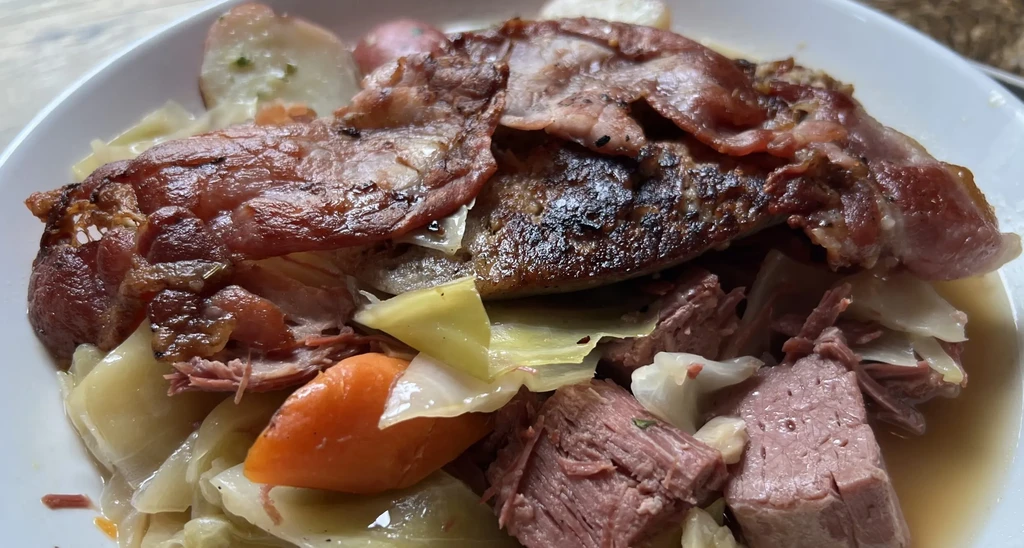 Close-up of braised beef, cabbage, carrots, potatoes in a white bowl.