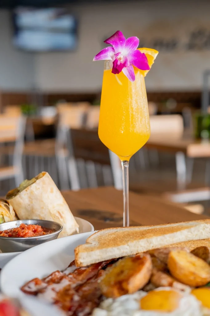 Vibrant orange drink with orchid, orange slice, and breakfast foods.