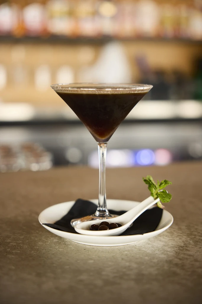 Dark cocktail in martini glass, garnished with coffee beans and mint.