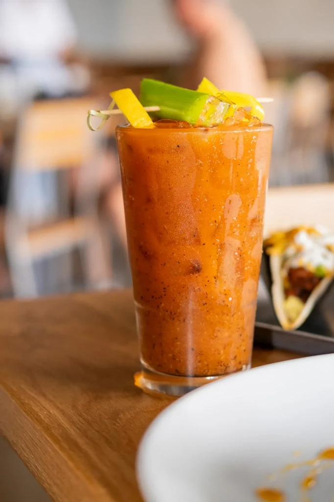 Orange blended drink garnished with peppers, with a blurred taco behind.