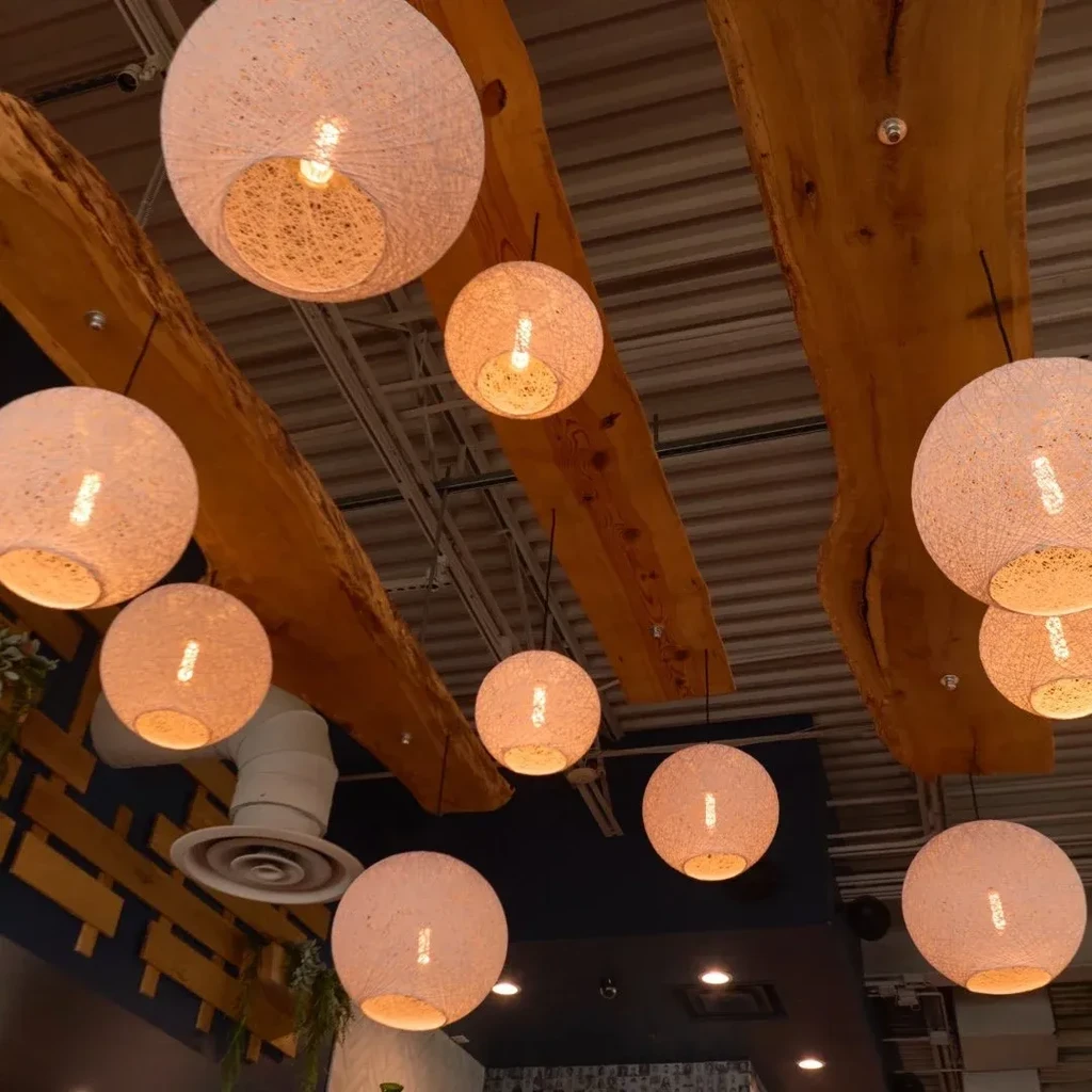 Woven spherical pendant lights below live-edge wooden beams and exposed ceiling.