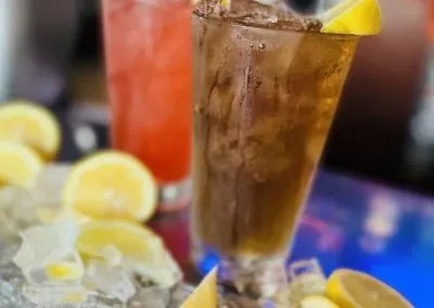 Amber and pink drinks with ice and lemon on a blue bar.