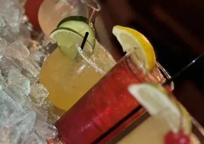 Three colorful garnished drinks with straws on crushed ice.