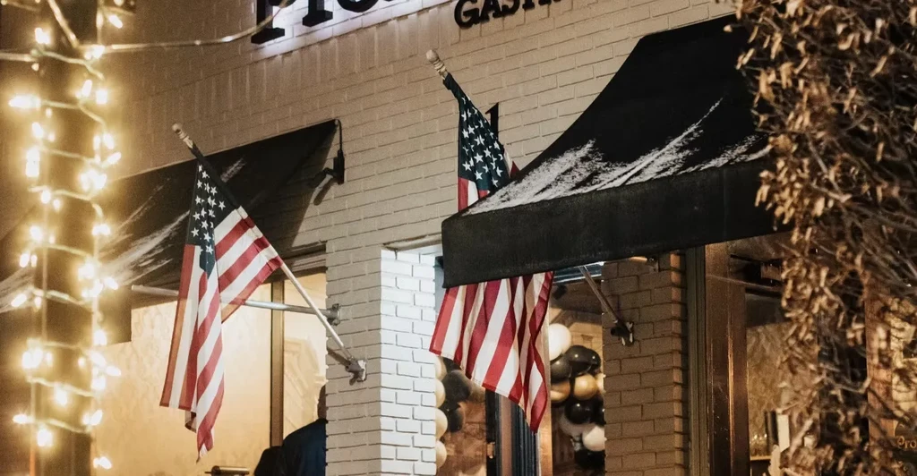 Nighttime brick gastropub with flags, awnings, and glowing string lights.