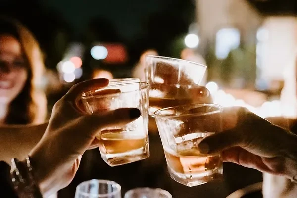 Three hands clinking glasses of amber liquid in a toast.